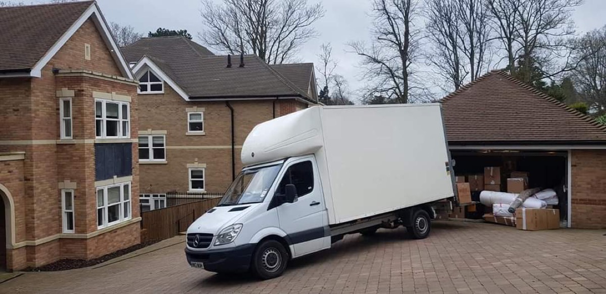 A Local Express Removals Luton van on a driveway beside a garage stacked with boxes and wrapped furniture ready to load